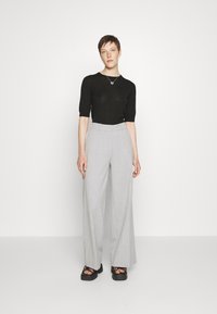 Black fitted short-sleeve top, light gray wide-leg trousers, and chunky black platform sandals; smooth fabric with a subtle texture.