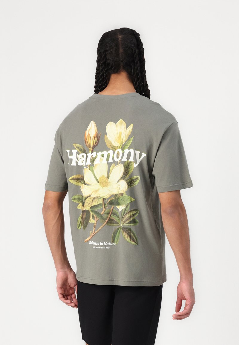 Grå bomulds t-shirt med korte ærmer og rund hals. Har et blomstermotiver og ordet "Harmony" på ryggen, med tekst nedenfor.