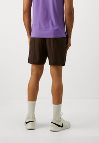 Bruna träningsshorts med en slät textur, i kombination med vita strumpor och ljusa skor med en svart swoosh, sedda bakifrån.