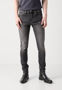 Šedé slim fit džíny z denimu s vybledlým efektem, pětikapsovým designem a kovovými doplňky. Kombinované s černými koženými kotníkovými botami.