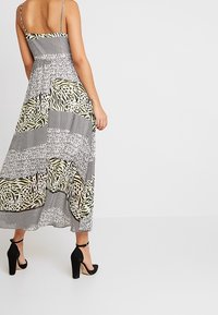 Maxiklänning i svart och vitt mönster med gröna accenter, justerbara axelband och en flödande silhuett. Passar bra med svarta klackar.