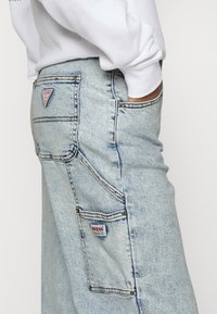 Ljusblå denimjeans med rak bendesign. Inkluderar flera fickor och en liten märkeslogotyp på ryggen.