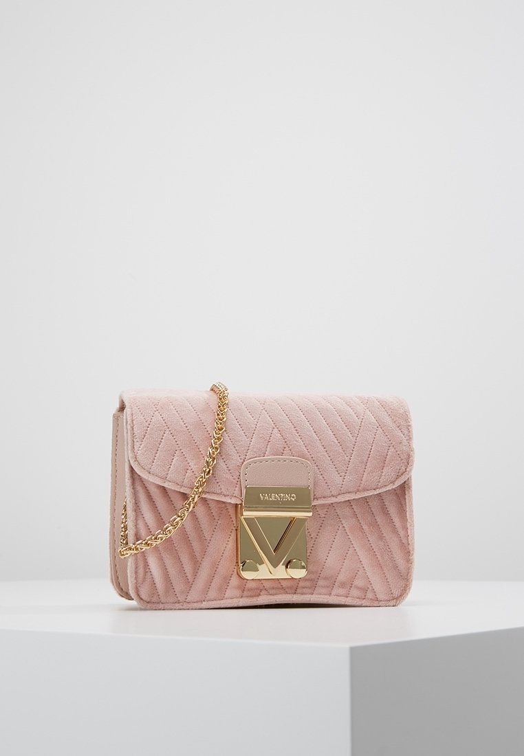 Borsa in suede rosa trapuntata con tracolla in catena dorata, dotata di una chiusura dorata con la lettera "V" e dettagli arrotondati. Forma rettangolare compatta.