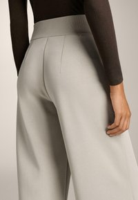 Svetlo sivi hlače širokih nogavica z rebrastim elastičnim pasom, ki imajo prilagojene šive za strukturiran videz in gladko teksturo.