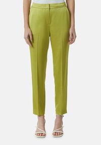Zielone satynowe spodnie o dopasowanym kroju, z plisami z przodu i gładką teksturą, w zestawieniu z białymi sandałami na paski.