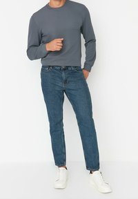Camisa gris de manga larga con textura acanalada, combinada con vaqueros azules y zapatillas blancas. El conjunto presenta un diseño casual y ajustado.