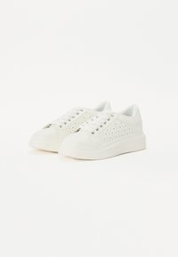 Hvite sneakers laget av glatt materiale med perforert design på sidene, med flate lisser, rund tå og en tykk, teksturert såle.