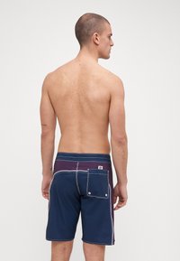Marina- och lila badshorts med vit söm. Utrustad med en bakficka med klaff och en logotypetikett på midjebandet. Platt midjebandsdesign.