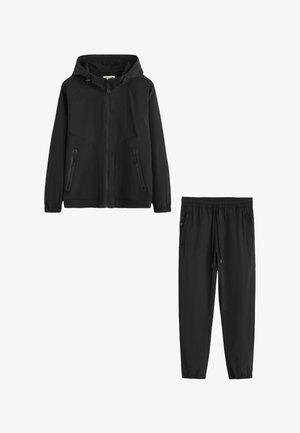 Veste noire à capuche avec fermeture éclair, poches latérales zippées et pantalon noir assorti avec cordon, poches zippées et poignets élastiques.