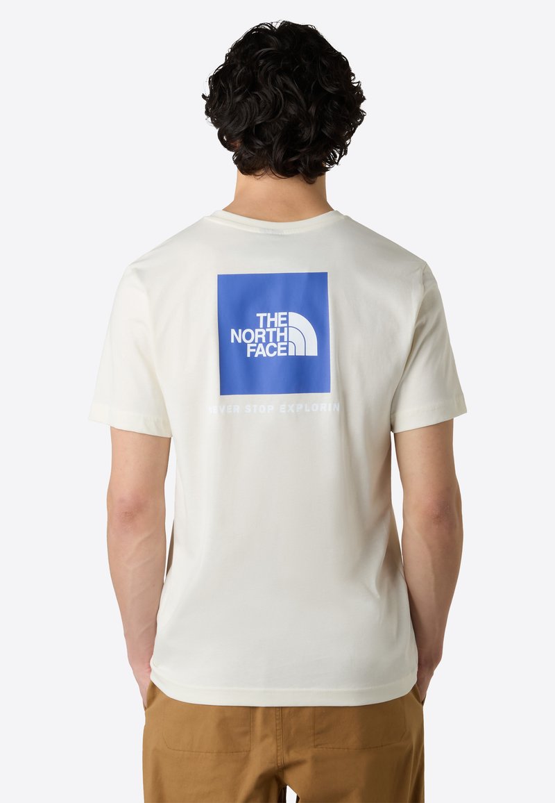 Cream-colored t-shirt featuring a blue logo square and text on the back. Cotton material with short sleeves and a crew neckline.