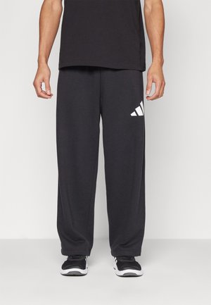 Black sweatpants with a loose fit, featuring a white adidas logo on the left thigh. Made from a soft, textured fabric for comfort.