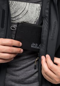 Portafoglio nero realizzato con materiale resistente, caratterizzato da una superficie texturizzata e dal logo 'Jack Wolfskin', tenuto all'interno di una tasca di giacca.