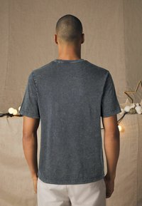 Grå kortærmet t-shirt, blød tekstur, afslappet pasform, synlig syning, rund hals og minimal falmønster. Enkel bagudsig.