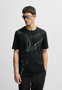 Black short-sleeve T-shirt with geometric light gray pattern, round neck, and logo on the front; worn with gray reflective sunglasses.