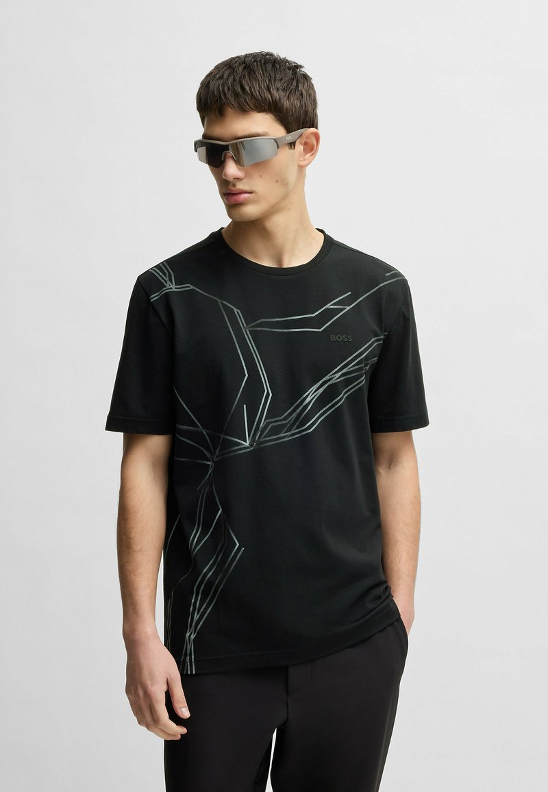 Black short-sleeve T-shirt with geometric light gray pattern, round neck, and logo on the front; worn with gray reflective sunglasses.