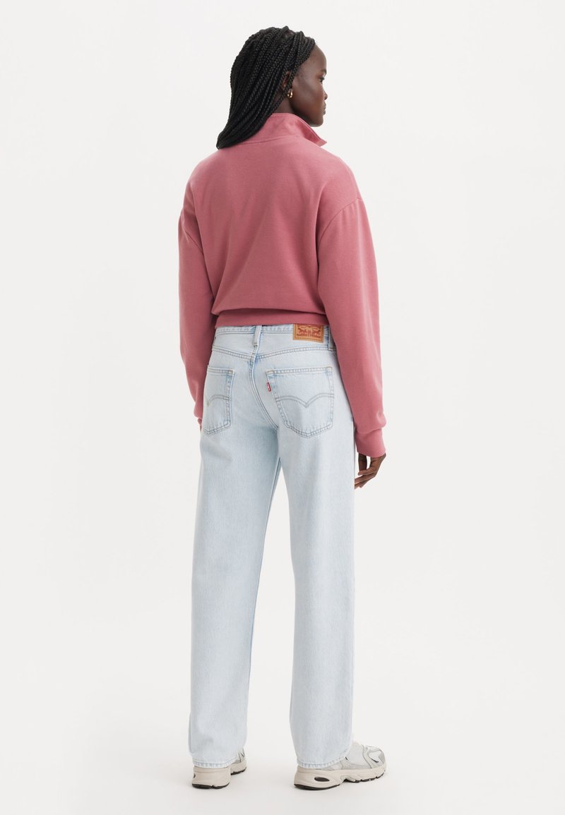 Felpa rosa a collo alto, accorciata, abbinata a jeans dritti azzurri chiari. Cuciture chiare e un'etichetta di pelle con marchio sui jeans.