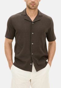 Brown short-sleeve shirt with a textured pattern, a notch collar, and five buttons, made from a soft material, displayed against a light background.
