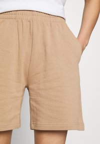 Beige bomullsshorts med elastisk midja och sidofickor. Slät textur och fållade kanter. Avslappnad passform.