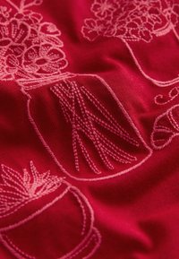 Tessuto rosso con ricamo rosa chiaro raffigurante composizioni floreali in barattoli e piante in vaso, con diverse texture e forme delle linee.