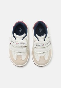 White and beige toddler sneakers with navy accents, double Velcro straps, and "TOMMY HILFIGER" branding on the strap. Size marked as 20.