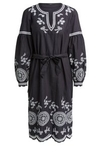 Robe noire avec broderies florales blanches et circulaires, décolleté en V, manches bouffantes et ceinture à nouer à la taille. Détail d'ourlet en biseau.