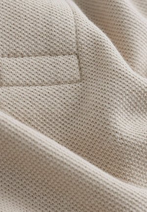 Material bej tricotat cu un model texturat, având un design subtil în formă de grilă. Textură moale, ușor pufoasă, cu o pliură la margine.