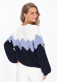 Sweter dzianinowy w białym, jasnoniebieskim i ciemnoniebieskim wzorze zygzakowym, z teksturowanym wykończeniem i ozdobnymi niebieskimi cekinami na rękawach.