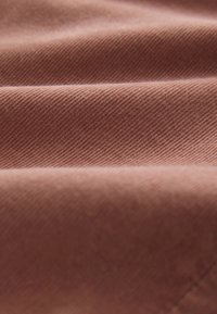 Rozsda színű szövet, sima, texturált felülettel és látható átlós szövési mintával, összehajtva és lágy redőket alkotva.