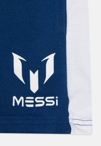 Zila un balta sporta auduma ar izteiktu baltu logotipu, kas sastāv no stilizētām formām; zem logotipa ir teksts "MESSi". Mīksta tekstūra.