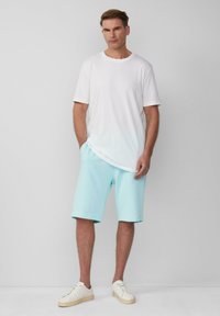Witte katoenen t-shirt met korte mouwen, gecombineerd met lichtblauwe katoenen shorts. Model draagt lichte sneakers. Eenvoudig en casual ontwerp.