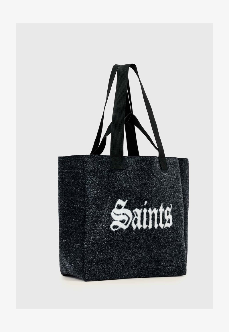 Czarna torba na ramię z filcu z kontrastującym białym napisem „Saints”, wyposażona w dwa czarne uchwyty z tkaniny i o strukturze w kształcie prostokąta.