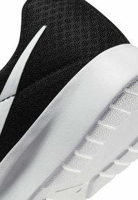 Gros plan d'une chaussure de sport noire en mesh avec une semelle blanche et un logo Swoosh blanc sur le côté.