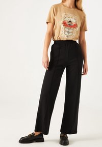 Camiseta gráfica beige con diseño floral, combinada con pantalones de pierna ancha negros de cintura alta y mocasines negros con detalles en dorado.