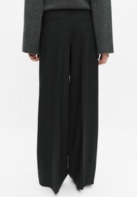 Szerokie czarne spodnie o gładkiej teksturze, dopasowanym kroju i dwóch tylnych kieszeniach. Posiadają subtelne zagniecenie biegnące wzdłuż każdej nogawki.