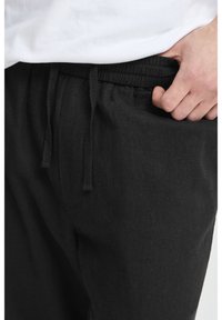 Black linen jogger pants with an elastic waistband and drawstring. Includes side pockets and a soft, textured fabric.