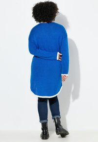 Lange, loszittende blauwe gebreide trui met witte afwerking bij de manchetten en onderrand, voorzien van een gestructureerde stof en een gebogen onderrand.