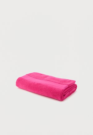 Serviette rose vif pliée à plat sur un fond blanc, montrant un tissu texturé et un détail de bande lisse.