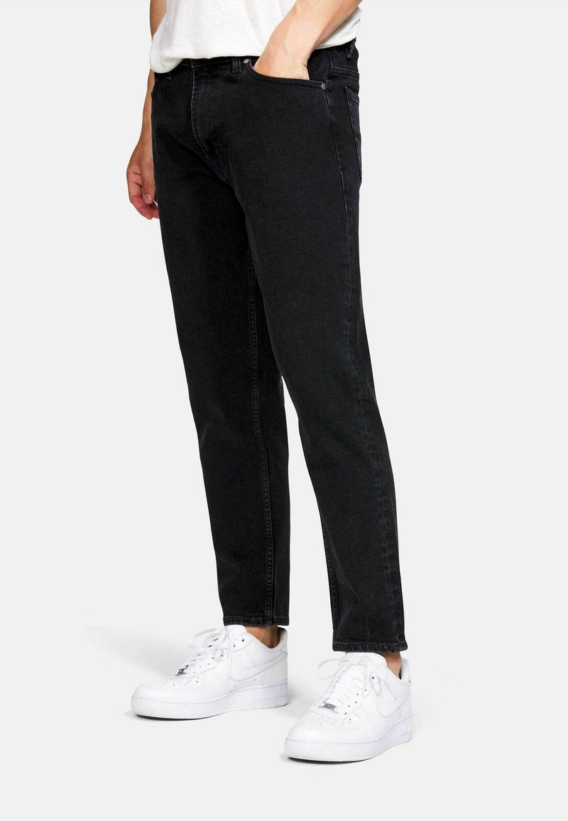 Vaqueros de mezclilla negros con un corte slim, que presentan un diseño clásico de cinco bolsillos y detalles de costura sutiles, combinados con zapatillas blancas.