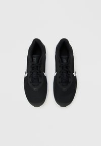 Para czarnych butów do biegania Nike z białymi logo swoosh i białymi podeszwami na jednolitym jasnym tle.