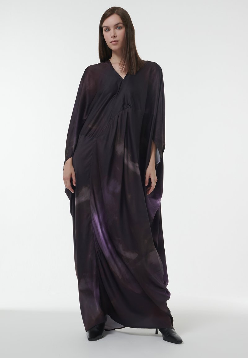 Lange, vloeiende jurk van donkerpaars fabric met een tie-dye patroon. Heeft een V-halslijn en brede mouwopeningen. Vloerlange ontwerp.