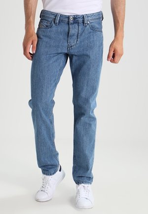 Jean en denim bleu clair avec une coupe droite, un design à cinq poches, fermeture à bouton et des détails de couture visibles, associés à des baskets blanches.