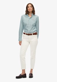 Jasnoniebieska koszula w paski z krótkim rękawem, z małym logo, białe dżinsy, brązowy pleciony pasek i ciemnoczerwone mokasyny. Gładkie faktury na całej powierzchni.