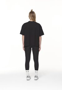 Černé oversize tričko s kleslými rameny, doplněné těsnými černými legínami. Obuv má světle šedý a bílý design s logovanými ponožkami.