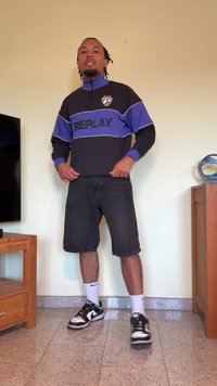 Svart och blå dragkedja sweatshirt med "REPLAY"-logotyp, tillsammans med knälånga denimshorts och svarta sneakers med vita accenter.
