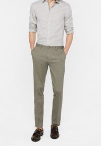 Ljusgrå linneskjorta, slim-fit olivgröna byxor och mörkbruna skor med spännen. Byxorna har framfickor och en enda knappstängning.