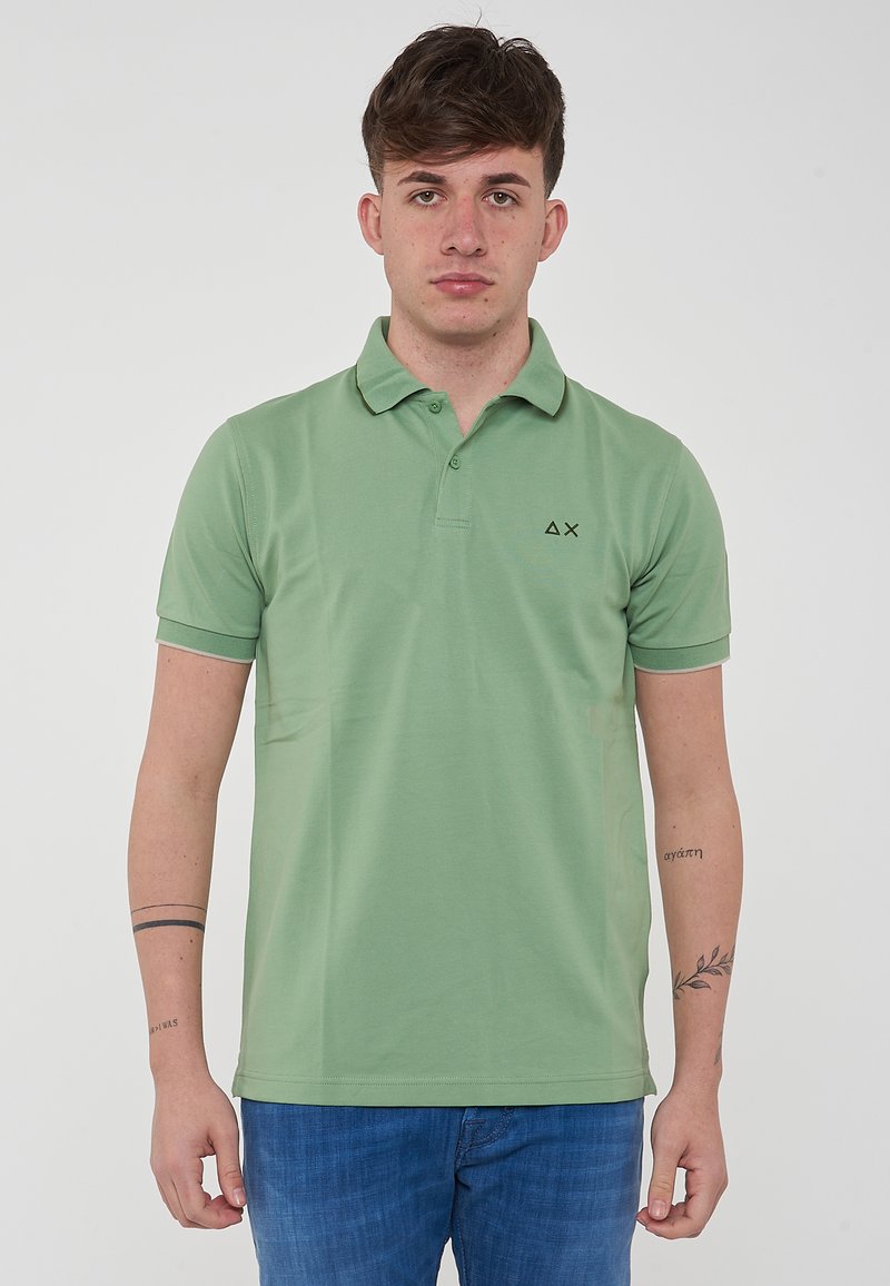 Polo verde realizzato in misto cotone, con colletto, maniche corte e un piccolo logo nero sul lato sinistro del petto. Morbida texture.