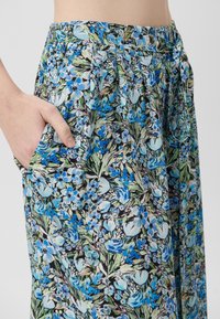 Blommönstrade byxor med ett blått och grönt mönster, tillverkade av lättviktigt tyg, med dragsko i midjan och sidofickor.