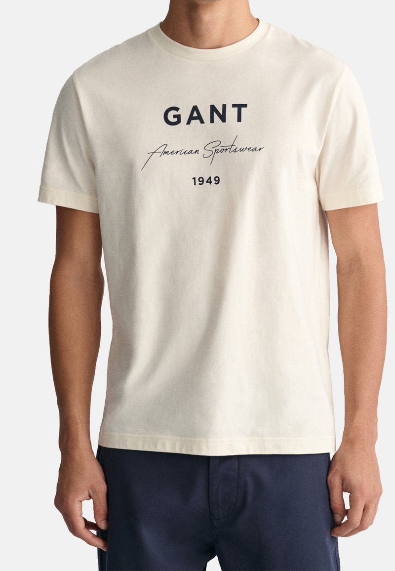 Kremové bavlněné tričko s námořnickým grafickým potiskem s nápisy "GANT American Sportswear" a "1949". Klasický kulatý výstřih a krátké rukávy.