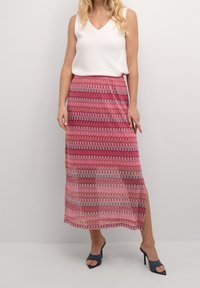 Maxi sukně v růžové a červené barvě s vlnitými vzory a bočním rozparkem, doplněná bílým bezramínkovým topem a tmavými podpatkovými muly.