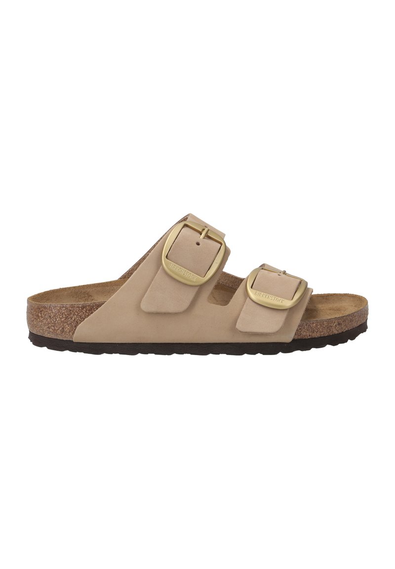 Sandale beige à deux brides avec une tige en suède doux, des boucles en métal doré, un semelle intérieure en liège et une semelle en caoutchouc texturé.